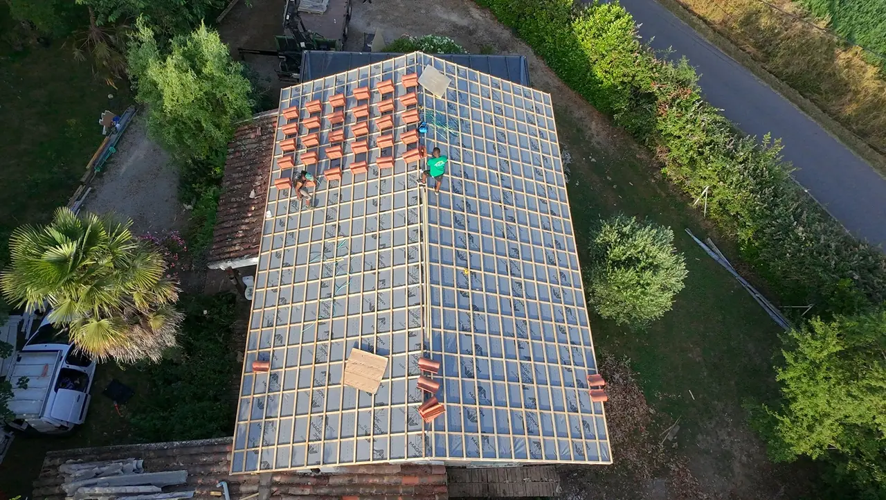Pose des liteaux et des premières tuiles sur une toiture, vue du ciel